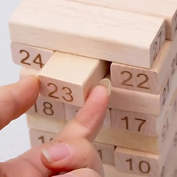 A hand carefully pulling a numbered wooden block from a tall tumbling tower stack during a game.